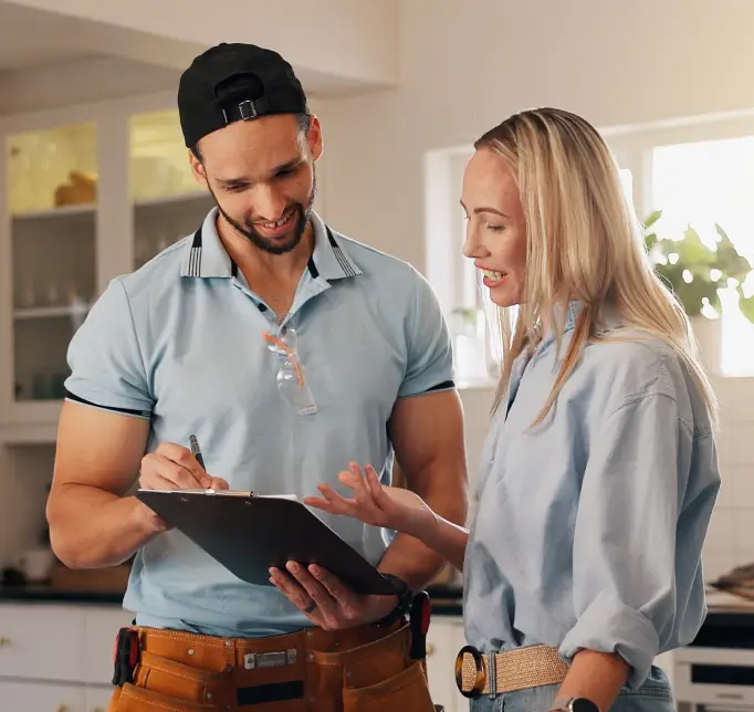 Man and woman in casual work clothes review plans on a clipboard in a bright kitchen.